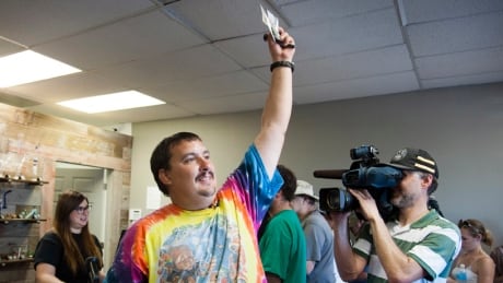 CORRECTS NAME TO BOYER, INSTEAD OF BOYD - Mike Boyer turns to the crowd outside, showing off the 4 grams of marijuana he bought as the first in line to legally purchase marijuana at Spokane Green Leaf, Tuesday, July 8, 2014, in Spokane, Wash. Twenty months after voters legalized recreational cannabis for adults over 21, Washington state's first few licensed pot shops opened for business Tuesday, catering to hundreds of customers who lined up outside, thrilled to be part of the historic moment. (AP Photo/The Spokesman-Review, Dan Pelle) Mike Boyer Washington marijuana buyer Spokane, Washington