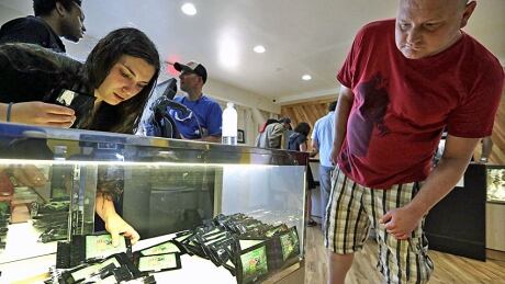 Clerk Havilah Nokes arranges packets of marijuana for sale as a customer peers in at the display at Cannabis City on the first day of legal recreational pot sales on July 8 in Seattle. By Friday, the shop had run out of product. hi-cannabis.jpg