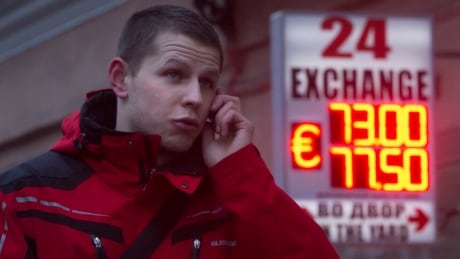 A man uses a mobile phone outside a display of a currency exchange office in St.Petersburg, Russia, Tuesday, Jan. 27, 2015. A day after a top ratings agency cut Russia�s rating to junk level, the government in Moscow on Tuesday announced a plan that will see the economy return to a budget surplus in 2017. Standard & Poor�s downgraded Russia�s rating to BB-plus late on Monday, a non-investment grade, for the first time since 2004, citing a slide in the ruble and weakening revenue from oil exports. The agency said Russia's financial system is weakening, limiting room for maneuver for Russia's Central Bank. (AP Photo/Dmitry Lovetsky) Russia Downgrade