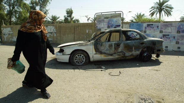 An Iraqi woman walks past a burnt car at the site where Blackwater guards who were escorting US embassy officials opened fire in the western Baghdad neighbourhood of Yarmuk.
