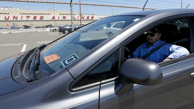 In this July 15, 2015 file photo, Uber driver Karim Amrani sits in his car parked near the San Francisco International Airport parking area in San Francisco. Uber said late Thursday it has settled a pair of major class-action lawsuits in California and Massachusetts that will keep its drivers independent contractors instead of employees.