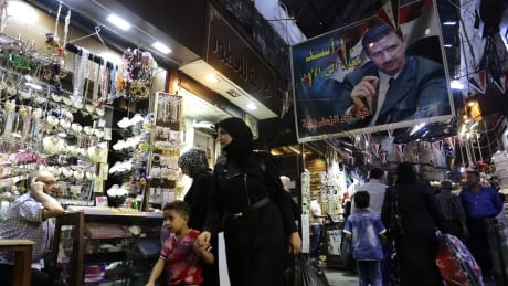 A poster of the Syrian President Bashar al-Assad, reading 'Assad is with you forever', hangs above shoppers at the popular Hamidiyeh market in Damascus. AFP_G21IK