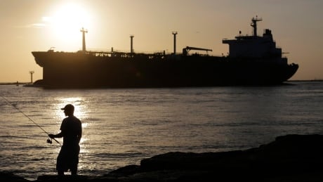 FILE - In this July 21, 2015, file photo, an oil tanker passes a fisherman as it enters a channel near Port Aransas, Texas, heading for the Port of Corpus Christi. The U.S., seemingly awash in crude oil after an energy boom sent thousands of workers scurrying to the plains of Texas and North Dakota, will begin exporting oil for the first time since the 1973 oil embargo. AP Explains US Oil Exports