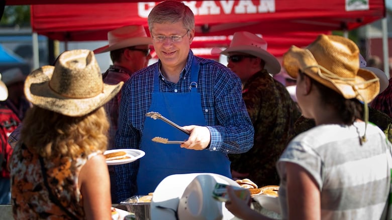 A man in a blue checked shirt and blue apron hands out pancakes under a red tent.