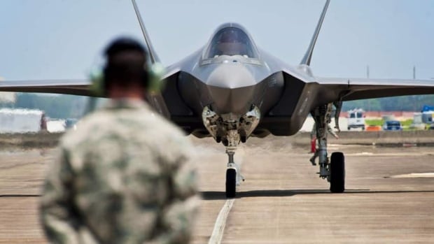 A man stands with his back to the camera, facing a fighter jet.