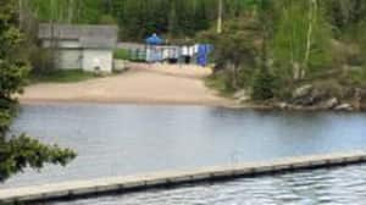 a blue lake with a sandy beach and a boardwalk across the water