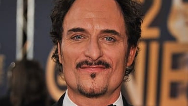 A dark-haired man with a goatee stands smiling in a black tux.