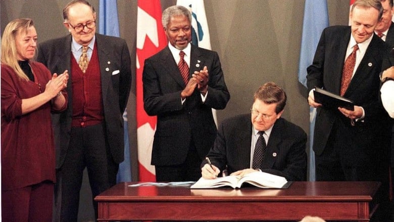 Four people watching a man sign a document