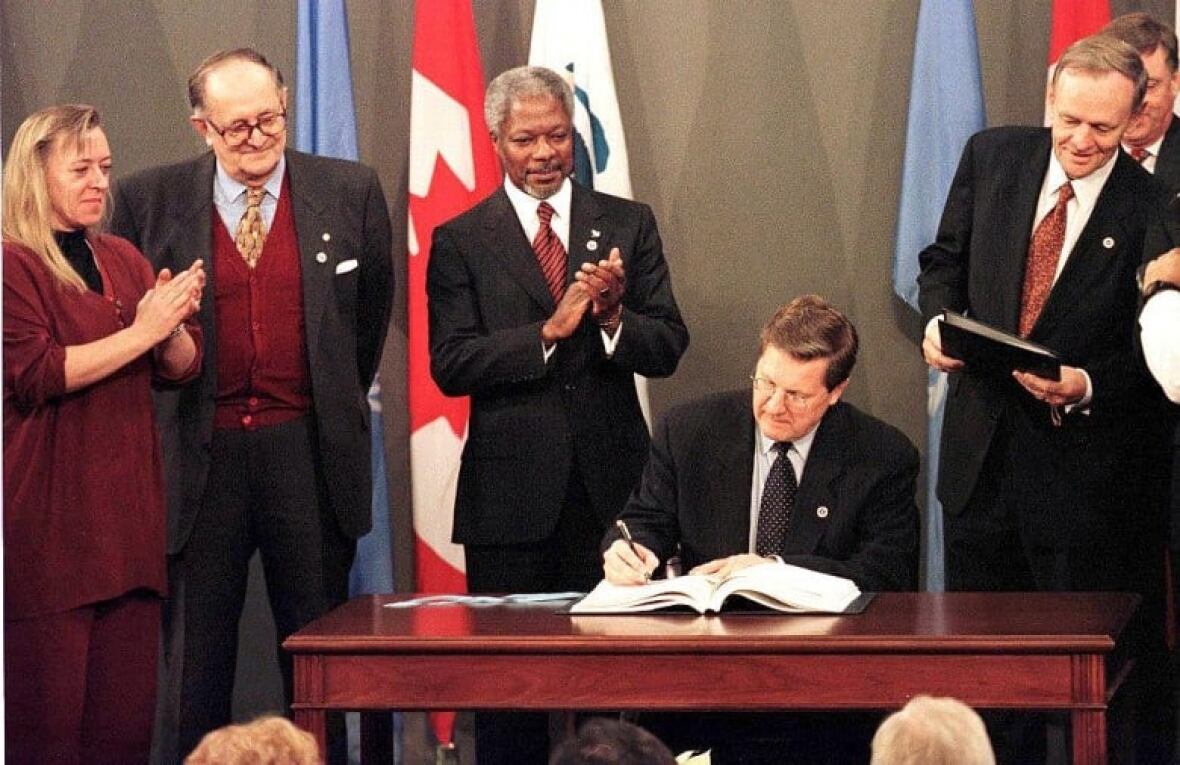 Four people watching a man sign a document