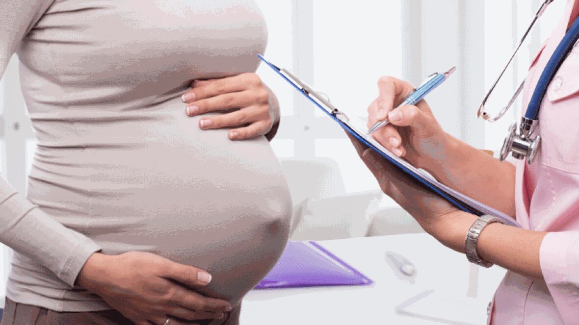 A pregnant person holds her abdomen with someone else writes on a clipboard