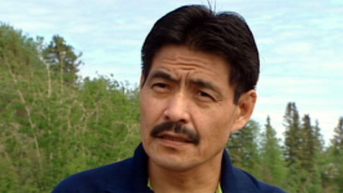 A man with a moustache stands outside.