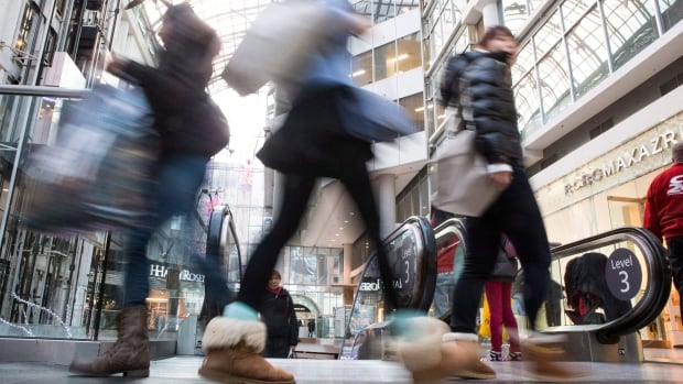 People walk past the camera, blurred from their movement, in a shopping mall.