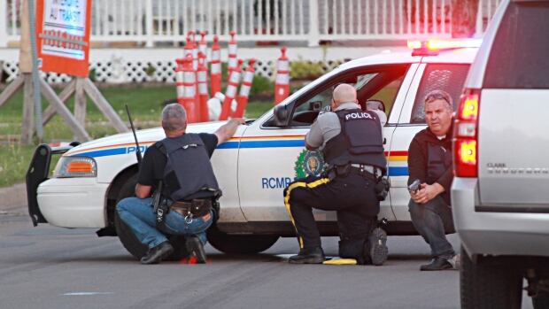 Police officers take cover behind their vehicles in Moncton during the shooting.