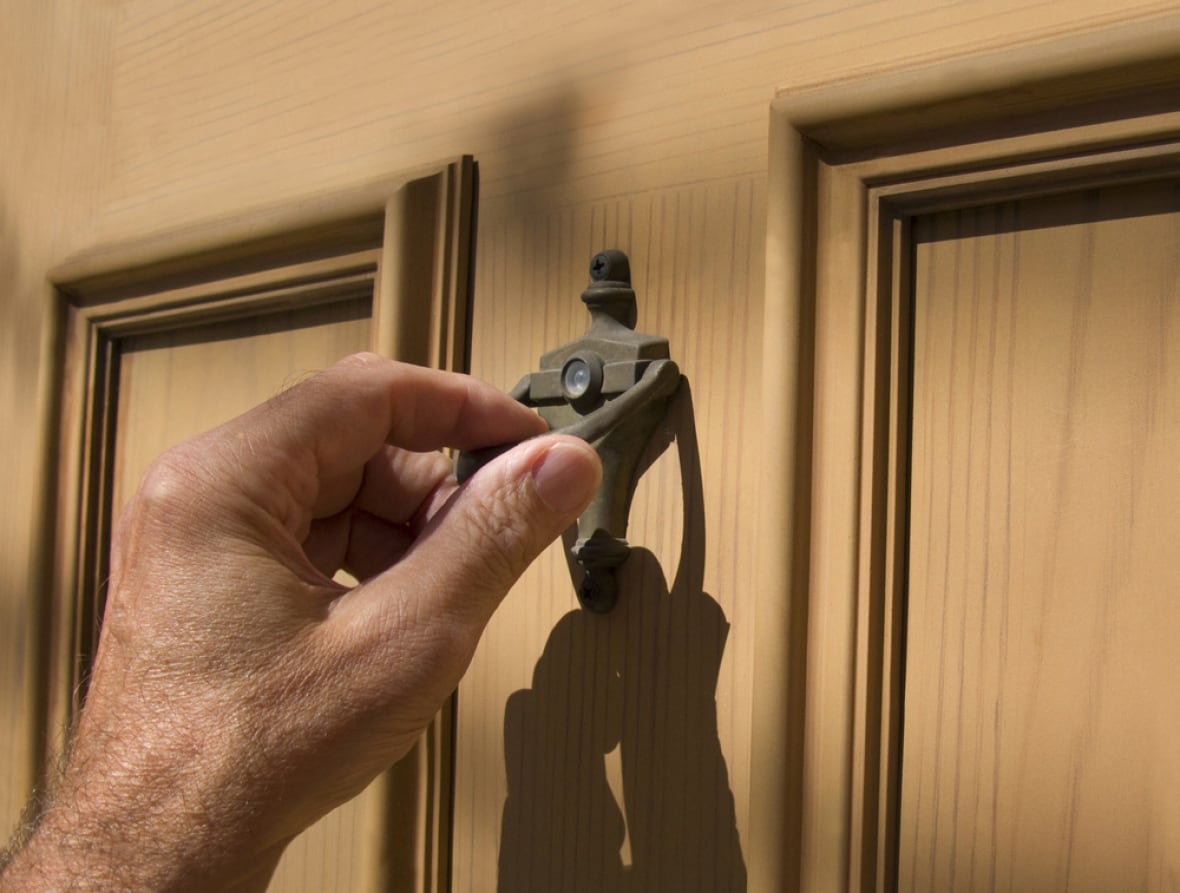 stock image of a hand holding a doorknocker on a door.