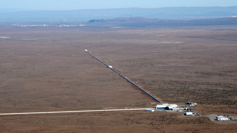 A building with two long metal arms stretch into an empty, dusty landscape. 