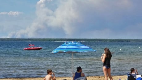 Saskatchewan sun bathers enjoy Waskesui beach in Prince Albert National Park, but smoke from forest fires billows on the horizon. waskesui beach prince albert saskatchewan
