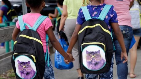 In this Aug. 15, 2015 file photo, students hold hands as they walk with their new book bags in Miami, Fla. In Ontario, students will be going back to school Tuesday with several labour disputes still happening. Back to School