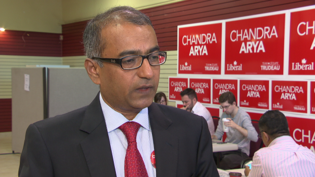 Liberal MP vying to be next prime minister dismisses importance of French language; A man with grey hair and glasses stands in a room with signs and people at desks\.