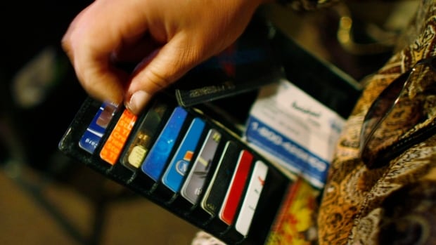 Consumer debt saw the biggest yearly increase in New Brunswick. The image shows a close-up of a person's hand holding a black wallet filled with multiple credit and membership cards.