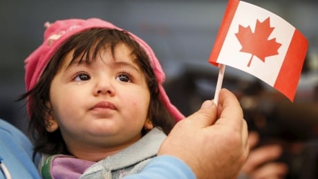 A Syrian refugee looks up as her father holds her and a Canadian flag as they arrive at Pearson Toronto International Airport in Mississauga, Ontario, December 18, 2015. CANADA-SYRIA/MIGRANTS