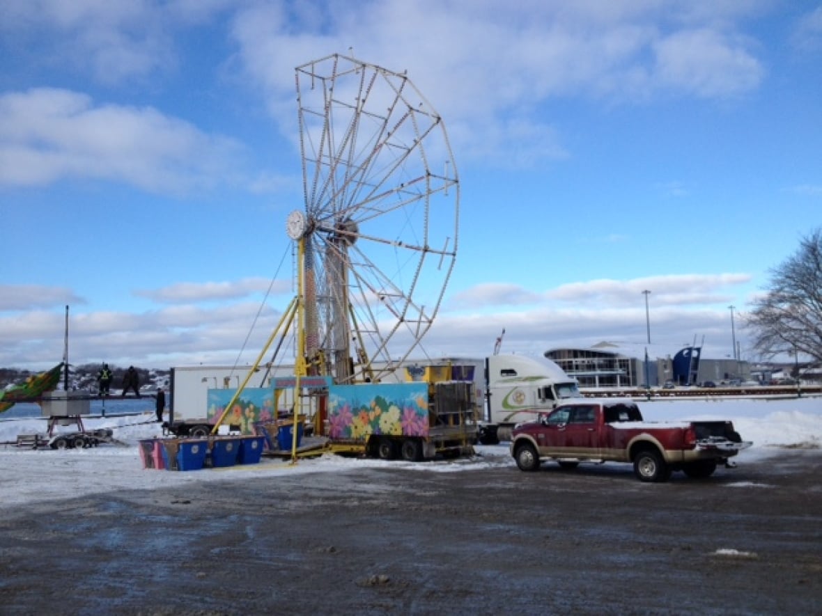 Half of a tall yellow ferris wheel is assembled amidst white snow and blue sky.
