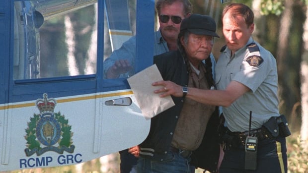 A police officer escorts a man out of a helicopter.