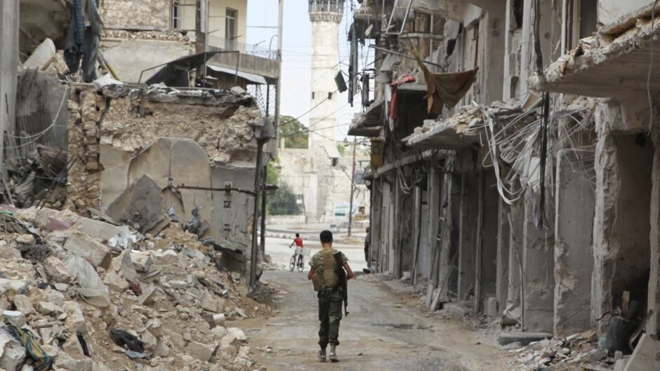 A Free Syrian Army fighter carries his weapon as he walks past damaged buildings in the old city of Aleppo, Syria in August 2015.