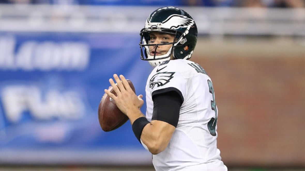 A quarter in a white jersey and a black football helmet holds the ball.
