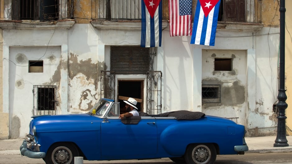 An old car passes by a house decorated with the flags of the United States and Cuba. EPA/ORLANDO BARRIA