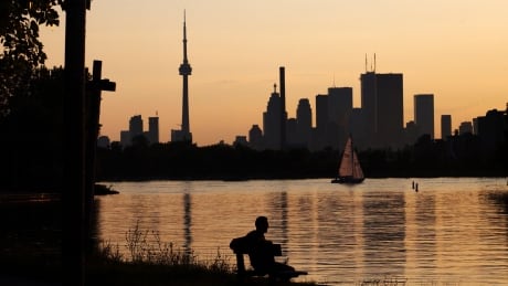 A man sits on a bench in front of the Toronto skyline during sunset at Ashbridge's Bay Park in Toronto, August 13, 2009. CANADA/