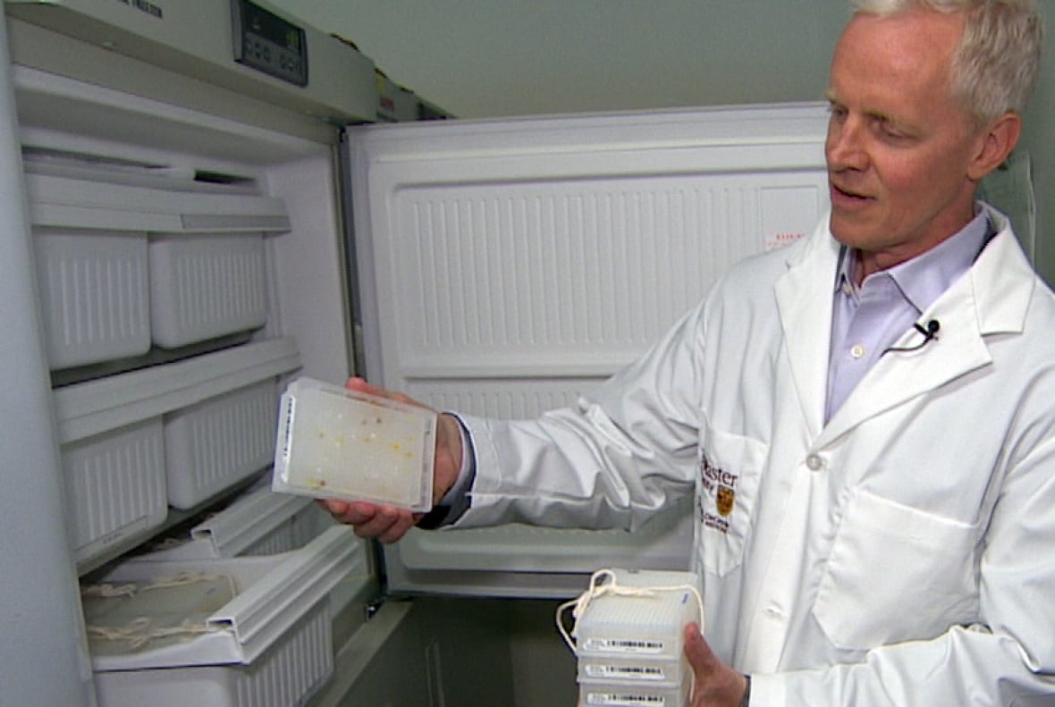 A male scientist wearing a lab coat holds samples in front of an open fridge. 
