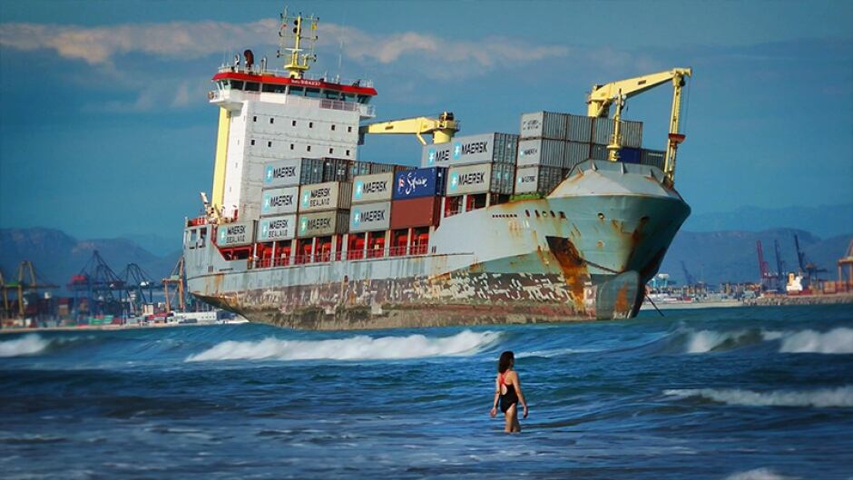 Swimmers share the beach with a rusty container ship