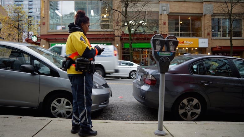 A woman wearing a yellow jacket writes a parking ticket