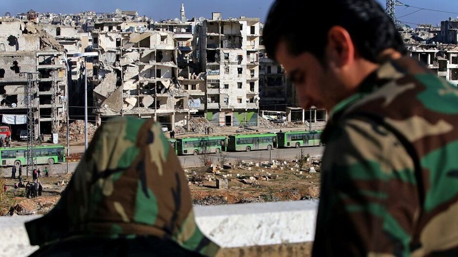 Pro-government forces watch as buses pass by during an evacuation operation of rebel fighters and their families from the embattled city of Aleppo.