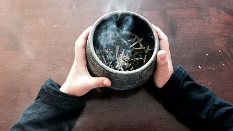 A child holds a bowl with burning sage — called smudging — it's an act that has become the subject of debate in Canada. Smudging