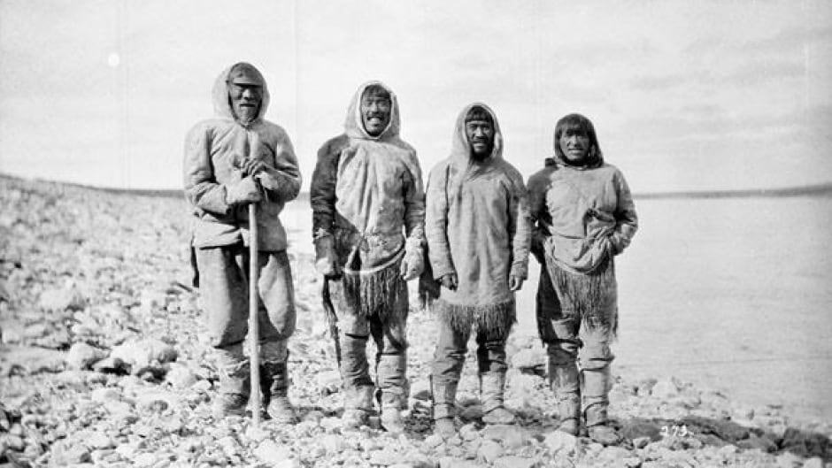 Four Inuit men standing by the shore, Baker Lake (Qamanittuaq), Nunavut. Heritage researcher Deborah Kigjugalik Webster says the names of these men are hard to find because the photograph is so old but continues her search.