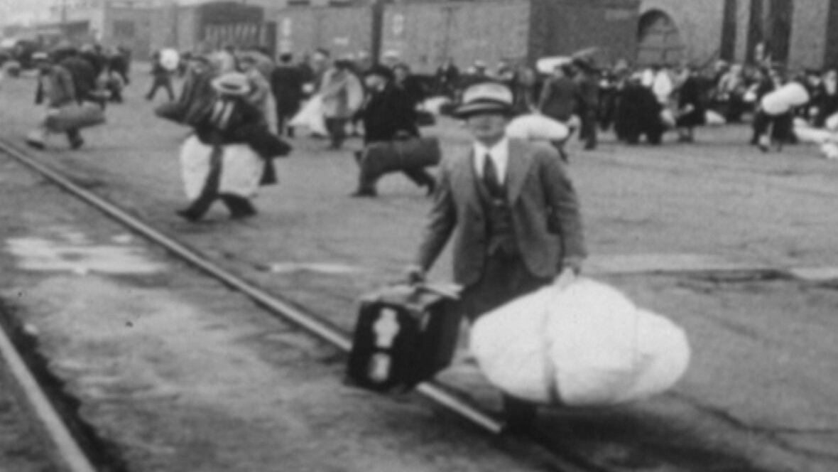 A man carries belongings in his hands as he crosses a set of street car tracks.