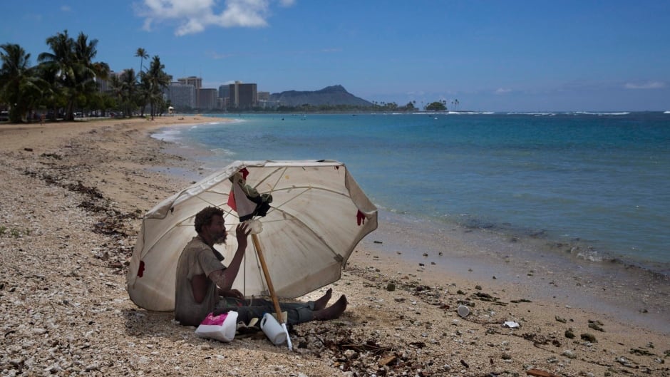 In this 2015 photo, a homeless man drinks water while sitting on the beach near Waikiki in Honolulu, Hawaii.