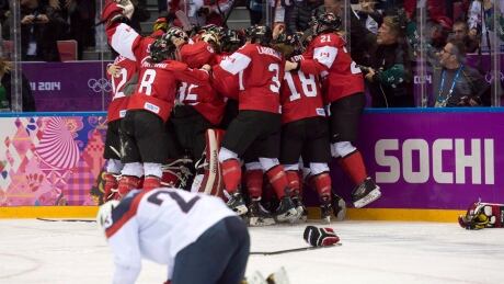 Team USA's Michelle Picard kneels on the ice as Team Canada celebrates their overtime win in the women's gold-medal hockey game at the Sochi Olympics in 2014. canada-usa
