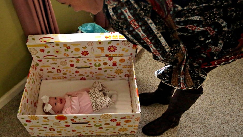 A mother checks on her three month-old daughter as she wakes up from a nap inside her "baby box".