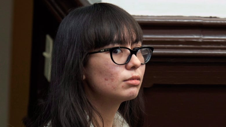 A woman with dark hear, wearing glasses and a white sweater, gives side-eye to the camera.