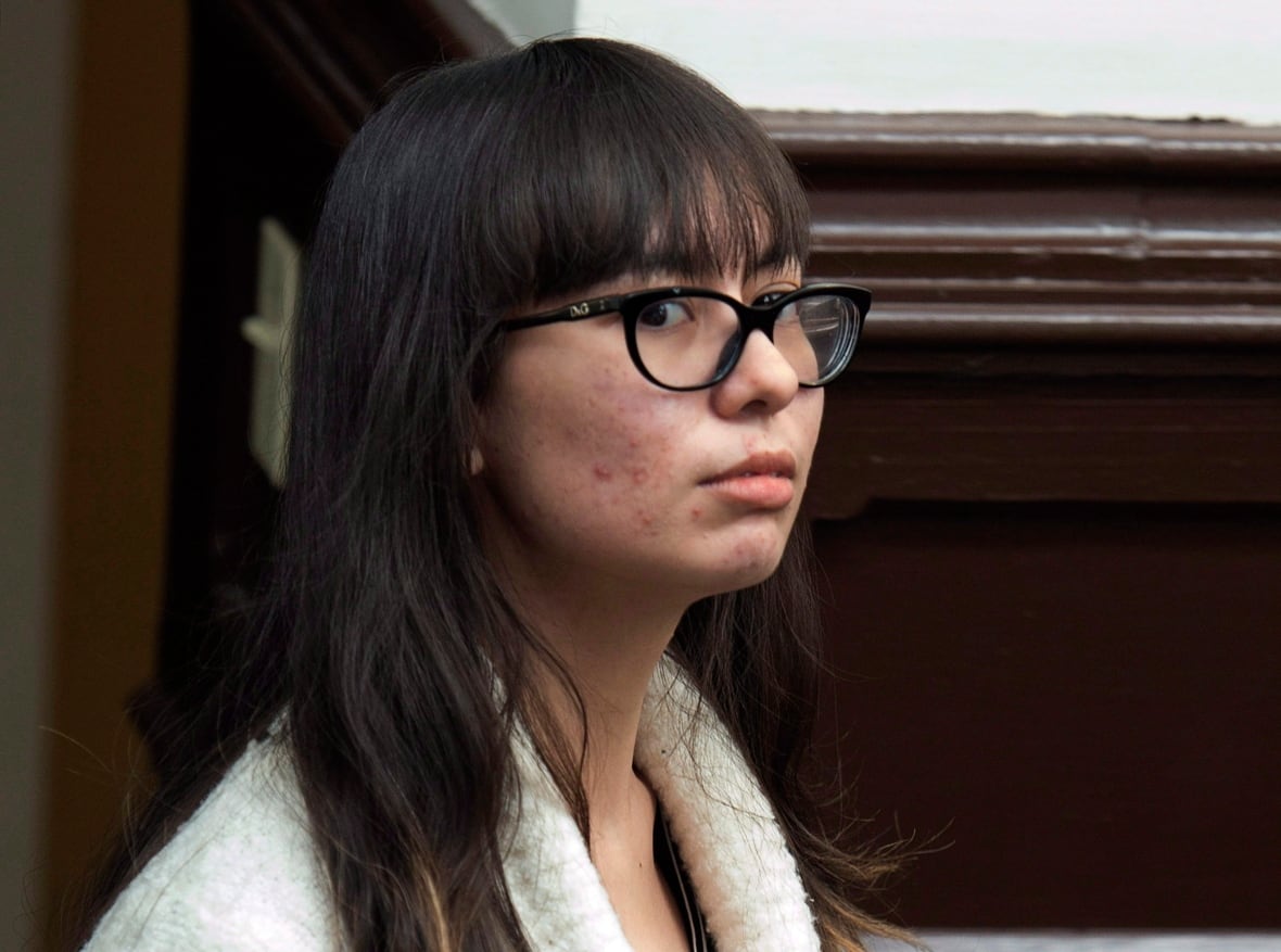 A woman with dark hear, wearing glasses and a white sweater, gives side-eye to the camera.