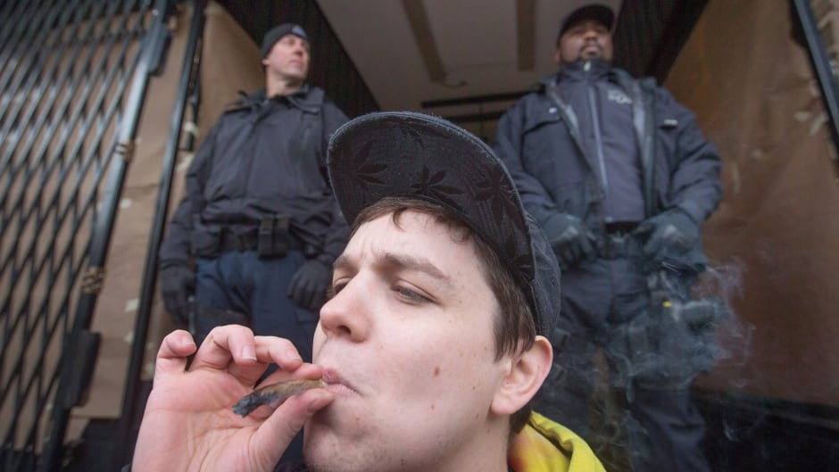 A young man smokes a joint as police officers stand outside the Cannabis Culture shop during a police raid in Vancouver, B.C. on Thursday March 9, 2017. THE CANADIAN PRESS/Darryl Dyck