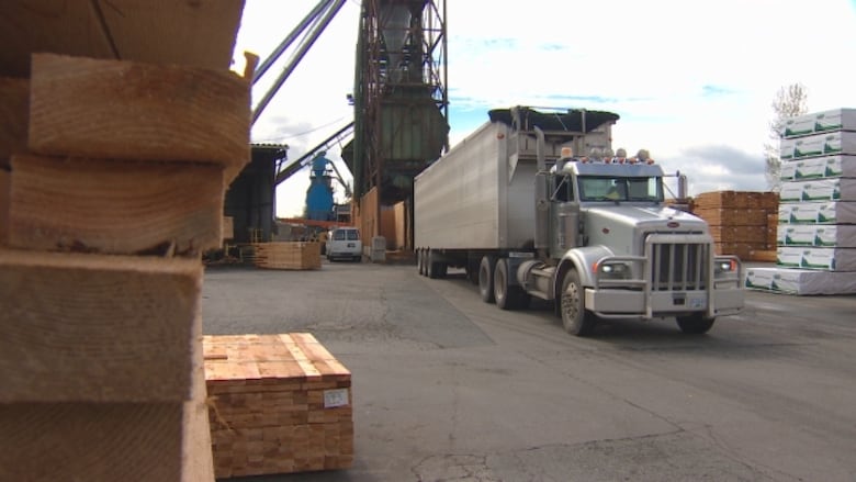 a truck carrying lumber drives past a pile of lumber