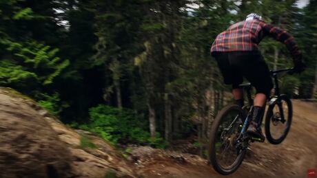 The expert rider clears the lip of the rock behind him and prepares to land on the trail below. A Line Whistler bike park