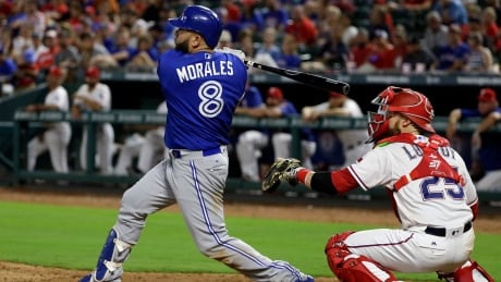 Toronto Blue Jays' Kendrys Morales follows through on a run-scoring single as Texas Rangers' Jonathan Lucroy, right, watches in the ninth inning. blue-jays