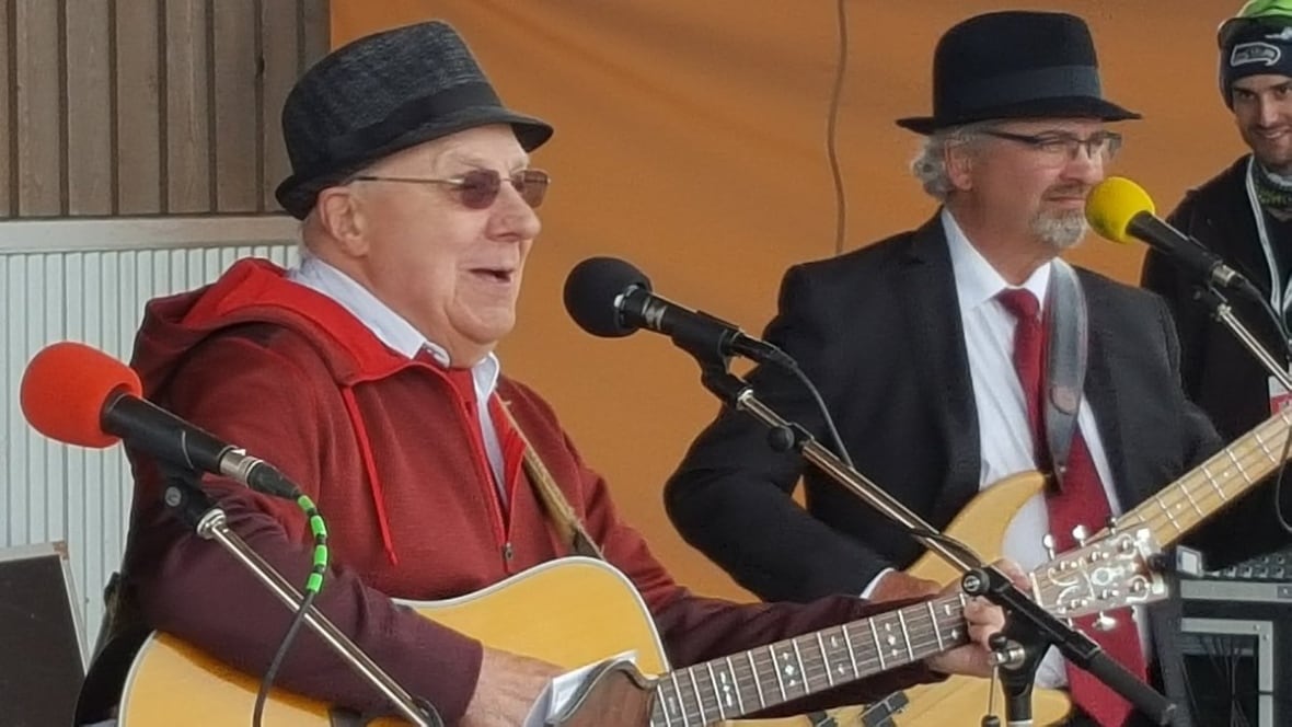 Two older men in hats performing with guitars on stage.