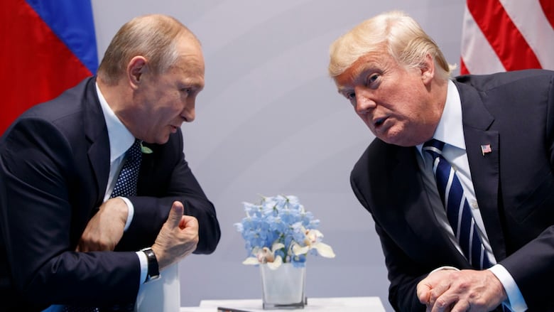 Two men, sitting on opposite sides of a table, lean in close to speak. 