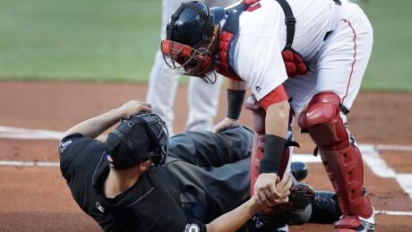Boston Red Sox catcher Christian Vazquez aids home plate umpire Chris Segal after he was accidentally hit on the head by Toronto Blue Jays' Josh Donaldson's bat during the first inning Monday in Boston. red-sox