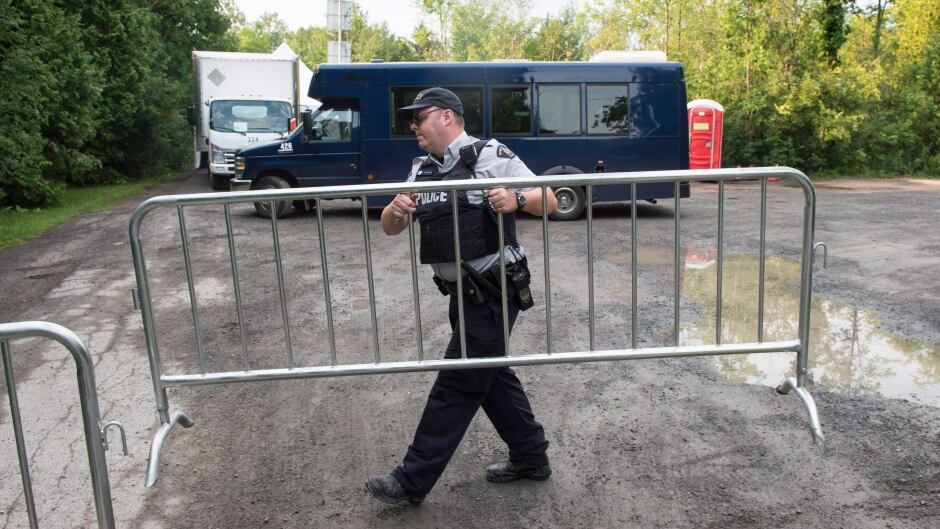An RCMP officer moves a barricade as they wait for the arrival of asylum seekers crossing the border into Canada from the United States at a police checkpoint close to the Canada-U.S. border near Hemmingford, Que., on Thursday, August 3, 2017.